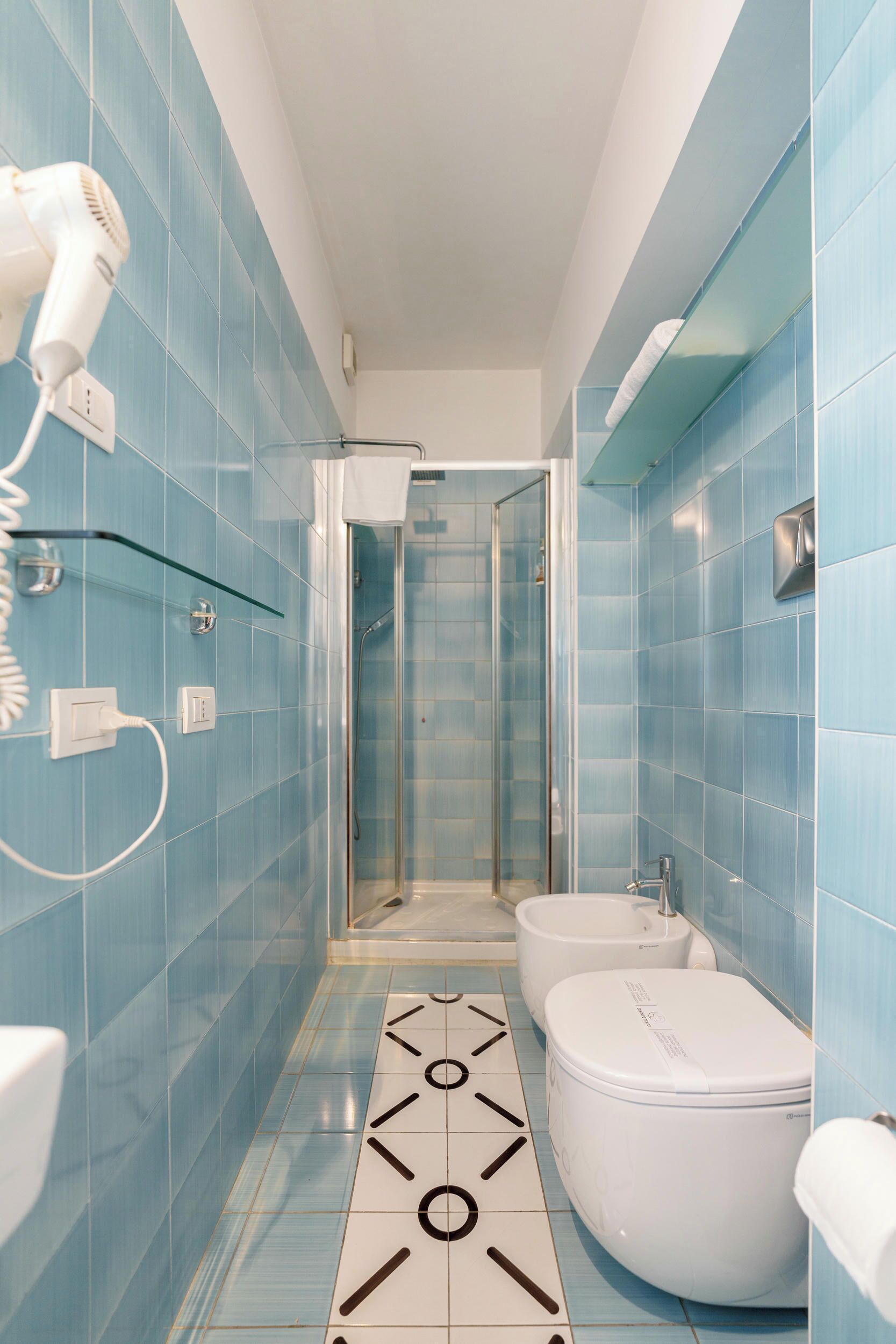 Een badkamer met blauwe tegels, een wit toilet, een bidet en een haardroger aan de muur.
