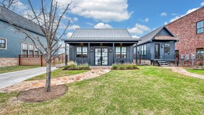 A modern two-story house with a stone pathway leading to the front door, surrounded by a well-maintained lawn and a tree. - DogTrot Hotel Suite A (Waco)