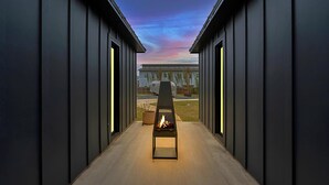 A corridor with a fire feature, leading to a building with a view of a trailer and a grassy area. - DogTrot Hotel Suite A (Waco)