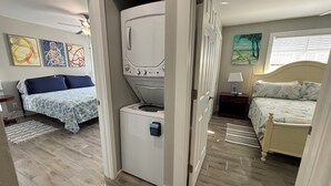 A compact room with a bed, a washing machine, and a small table with a lamp.