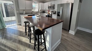 A modern kitchen with white cabinets, stainless steel appliances, and a wooden island with bar stools.