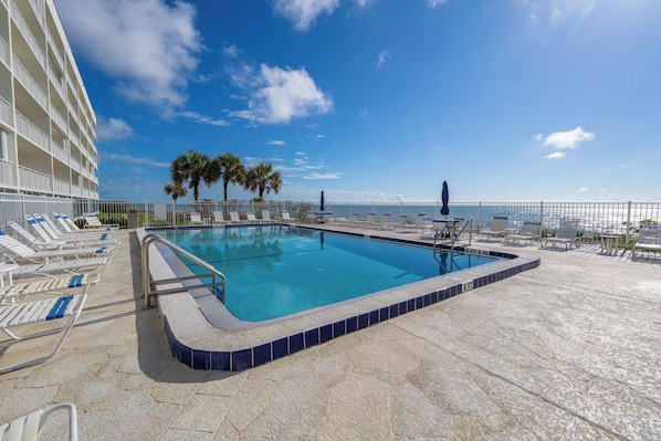 A swimming pool with lounge chairs, palm trees, and a view of the ocean.