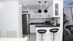 Una cocina moderna con armarios blancos, taburetes negros y un refrigerador de acero inoxidable.