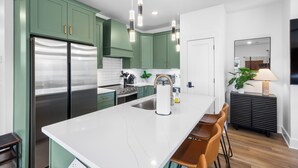 A modern kitchen with green cabinets, stainless steel appliances, and a white marble island.