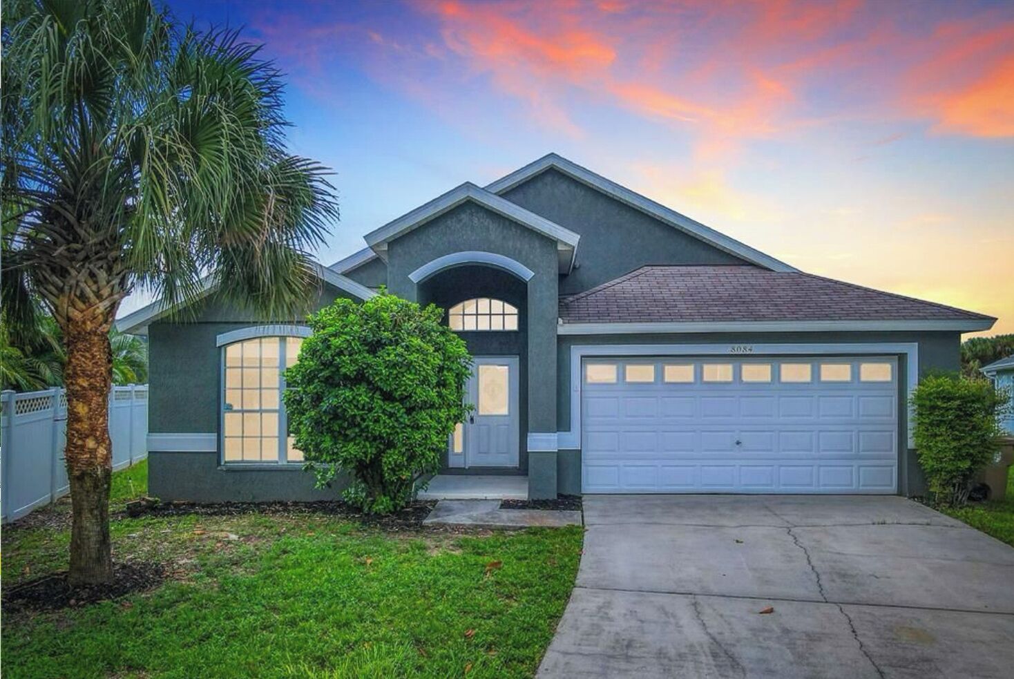A residential house with a garage, a front yard with a palm tree, and a driveway.