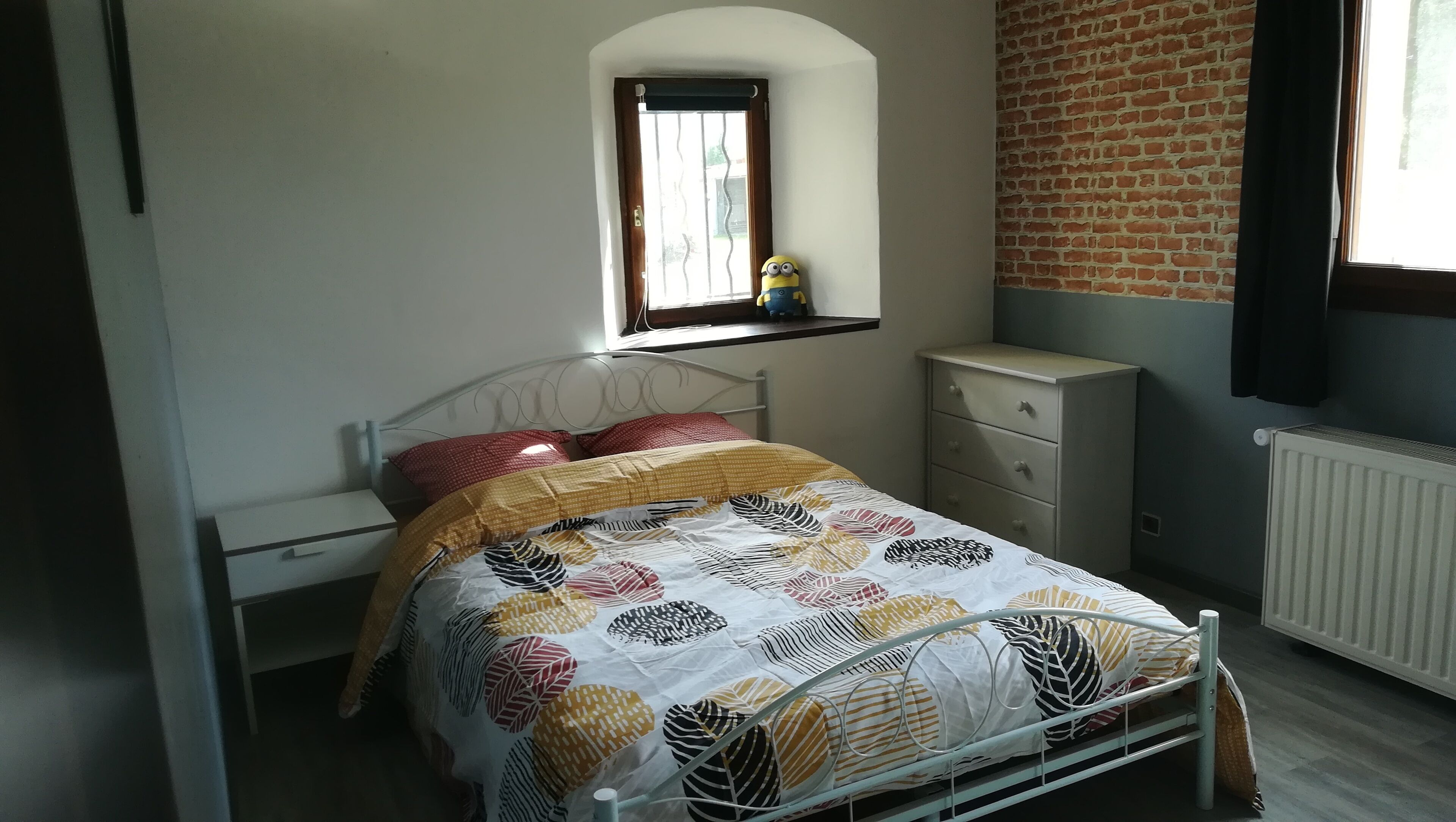 Una camera da letto con un letto, una finestra, un comò e un termosifone.