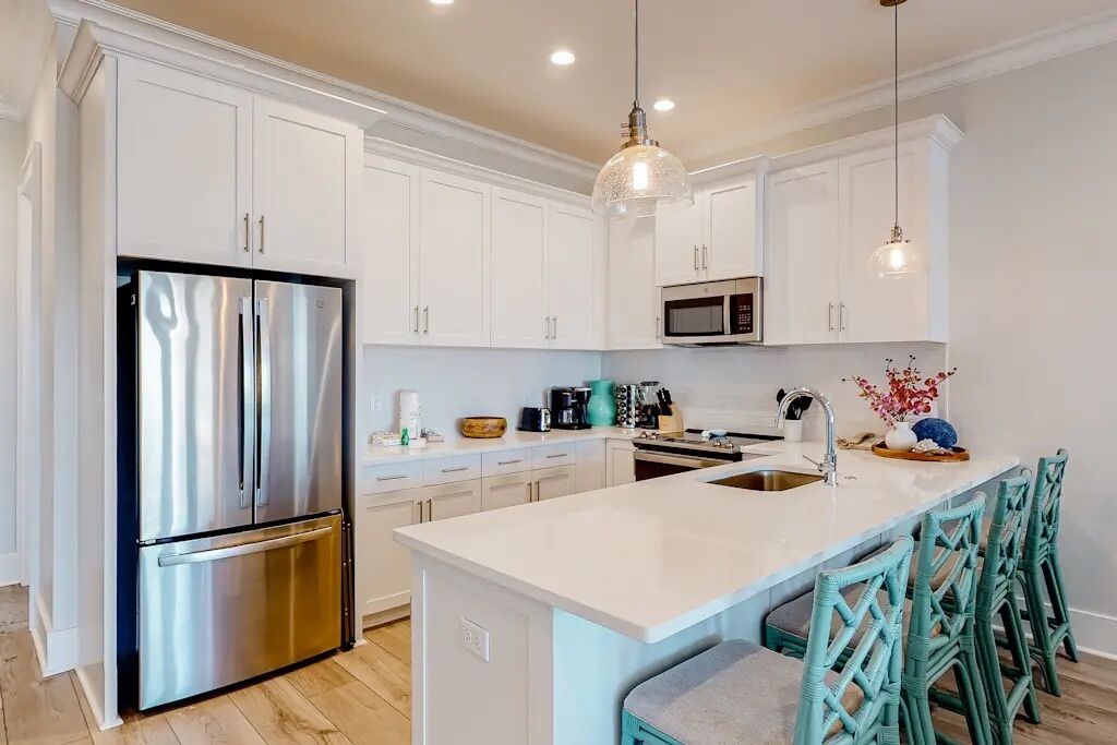 Una cocina moderna con armarios blancos, electrodomésticos de acero inoxidable y sillas color turquesa.