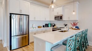 A modern kitchen with white cabinetry, stainless steel appliances, and teal chairs. - 50 Steps To Beach, Heated Pool, Hot Tub, Gulf View, Dog Friendly, Lost Dunes 4BR (Gulf Shores)