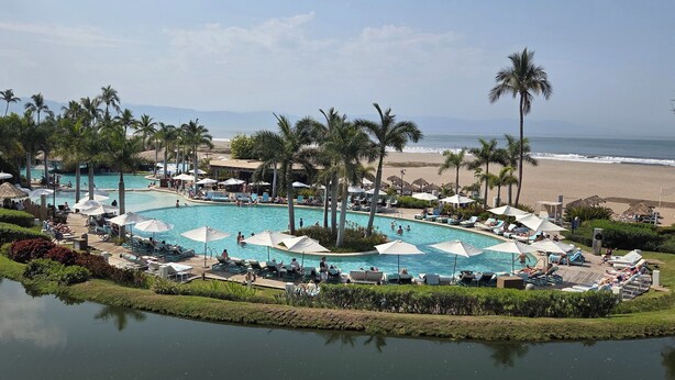 Ein Resort mit mehreren Swimmingpools, Palmen und Blick auf den Strand.