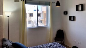 A bedroom with a bed, a window with curtains, an air conditioner, a hanging light fixture, and a chair. - Playa del Carmen Apartment (Playa del Carmen)