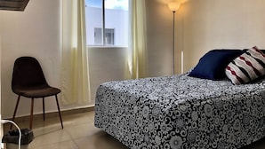 A bedroom with a bed, a chair, a window with curtains, an air conditioning unit, and a lamp. - Playa del Carmen Apartment (Playa del Carmen)