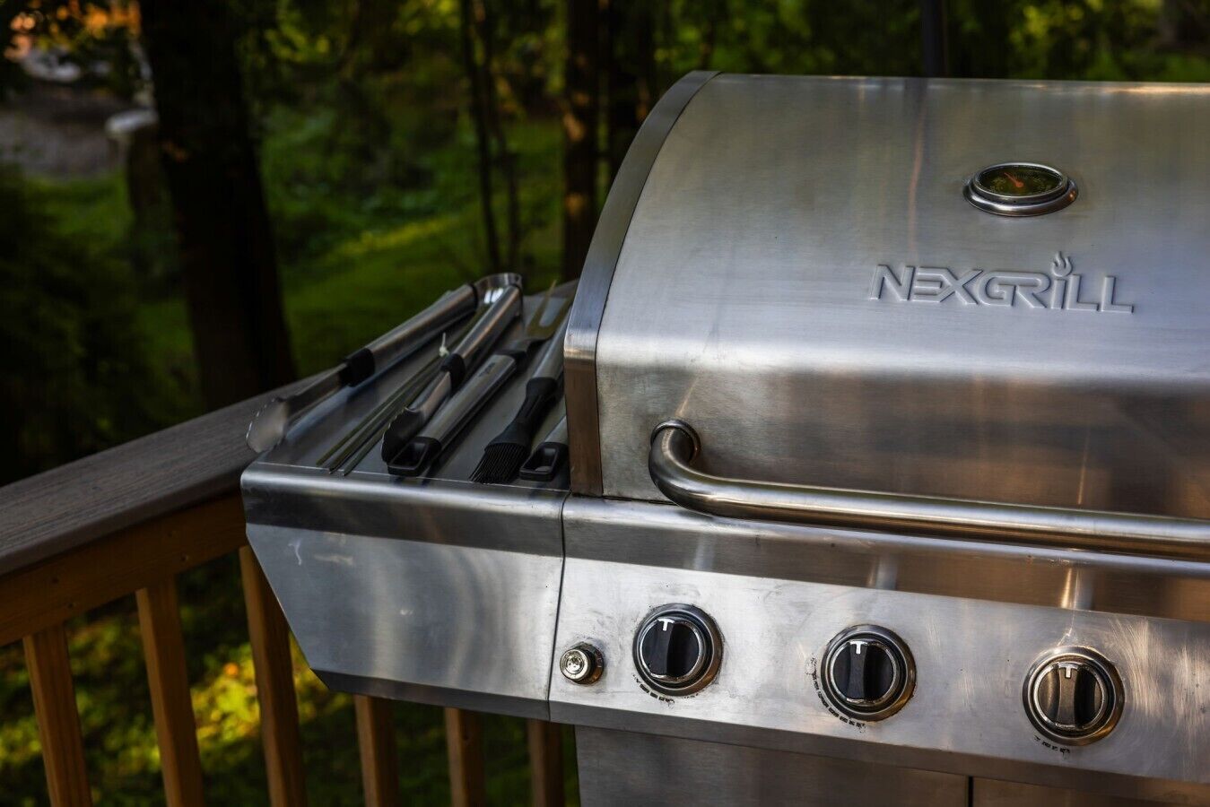 A stainless steel NexGrill barbecue with three control knobs and a handle, mounted on a wooden deck.