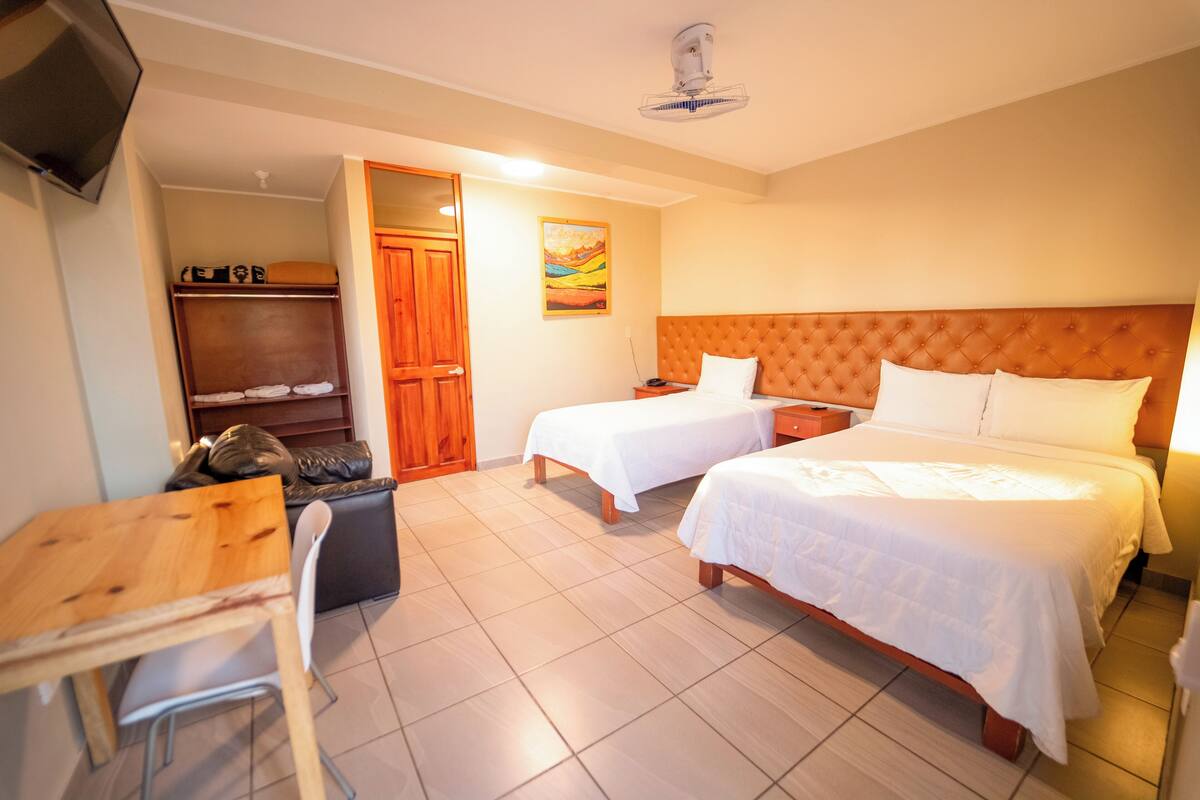 A hotel room with two beds, a wooden desk, a chair, a wardrobe, and a painting on the wall.