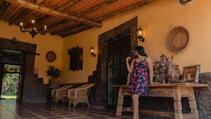 A spacious lobby with a tiled floor, a wooden table with decorative items, wicker chairs, and a stone wall. - Hotel Fundo San Rafael  (Nazca)