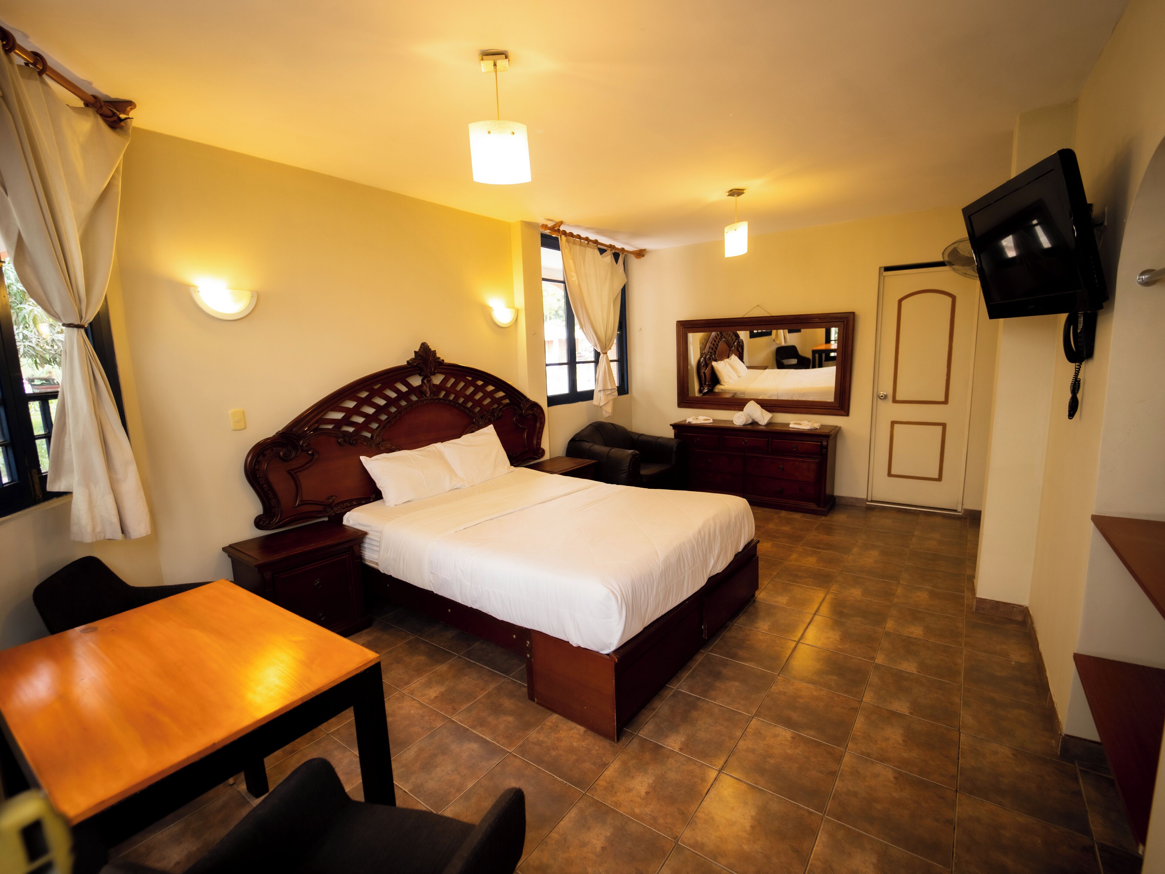 Ein Hotelzimmer mit Bett, Schreibtisch, Stuhl, Fernseher, Kommode und Spiegel.