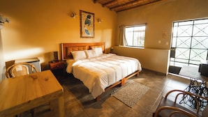 A bedroom with a wooden bed, a dining table, and chairs. There is a window with a view of the outside. - Hotel Fundo San Rafael  (Nazca)