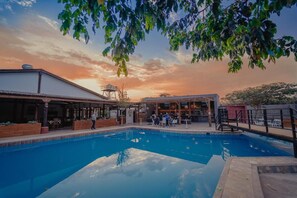 A swimming pool with a covered area, a water tower, and a bar/lounge area with people. - Hotel Fundo San Rafael  (Nazca)