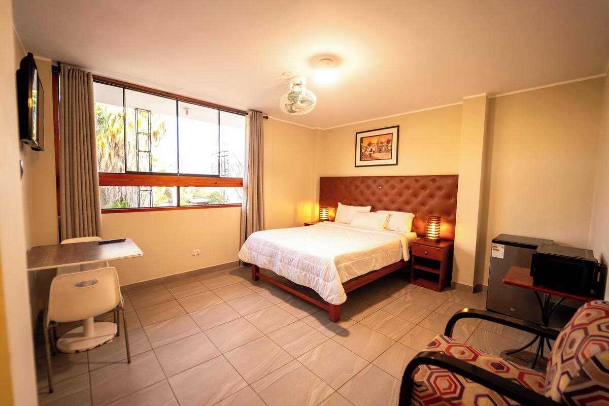 A hotel room with a bed, desk, chair, and a small kitchenette.