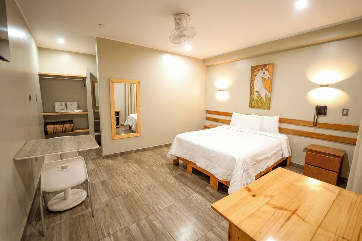 A hotel room with a bed, bedside table, chair, desk, and a wardrobe.
