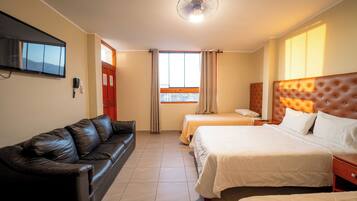 A hotel room with a leather sofa, two beds, a TV, and a window with curtains.