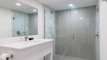 A modern bathroom with a white vanity, a glass shower enclosure, and a large mirror.