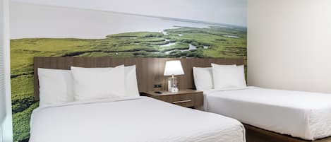 A hotel room with two beds, a nightstand with a lamp, and a large mural of a landscape.