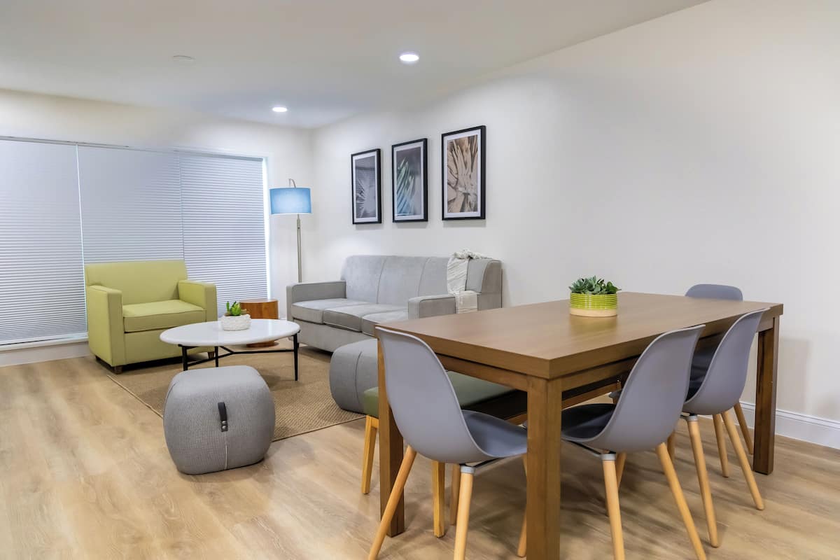 A modern living room with a wooden dining table, grey chairs, a grey sofa, a yellow armchair, and a floor lamp.
