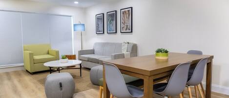 A modern living room with a wooden dining table, grey chairs, a grey sofa, a yellow armchair, and a floor lamp.
