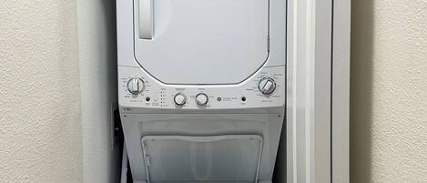 Una lavadora blanca y compacta de carga frontal en un lavadero pequeño con una puerta en un lateral.