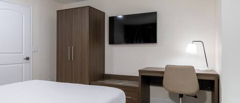 A bedroom with a bed, a wardrobe, a desk with a chair, and a flat-screen TV.