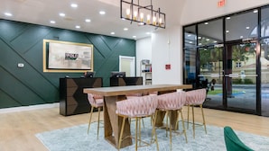 Una hall d'albergo moderna con un'ampia scrivania della reception in legno, pareti verdi e un tappeto a motivi.
