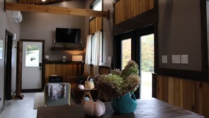 Un intérieur en bois avec une table à manger, un vase turquoise orné d’hortensias et un téléviseur fixé au mur.