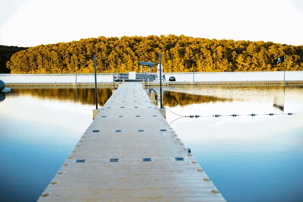 A pier extending into a calm body of water with a forested hill in the background.