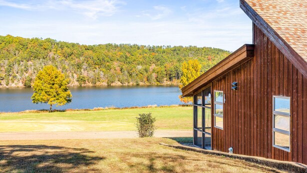 Een houten chalet met een groot raam, een klein terras en uitzicht op een meer en bos.