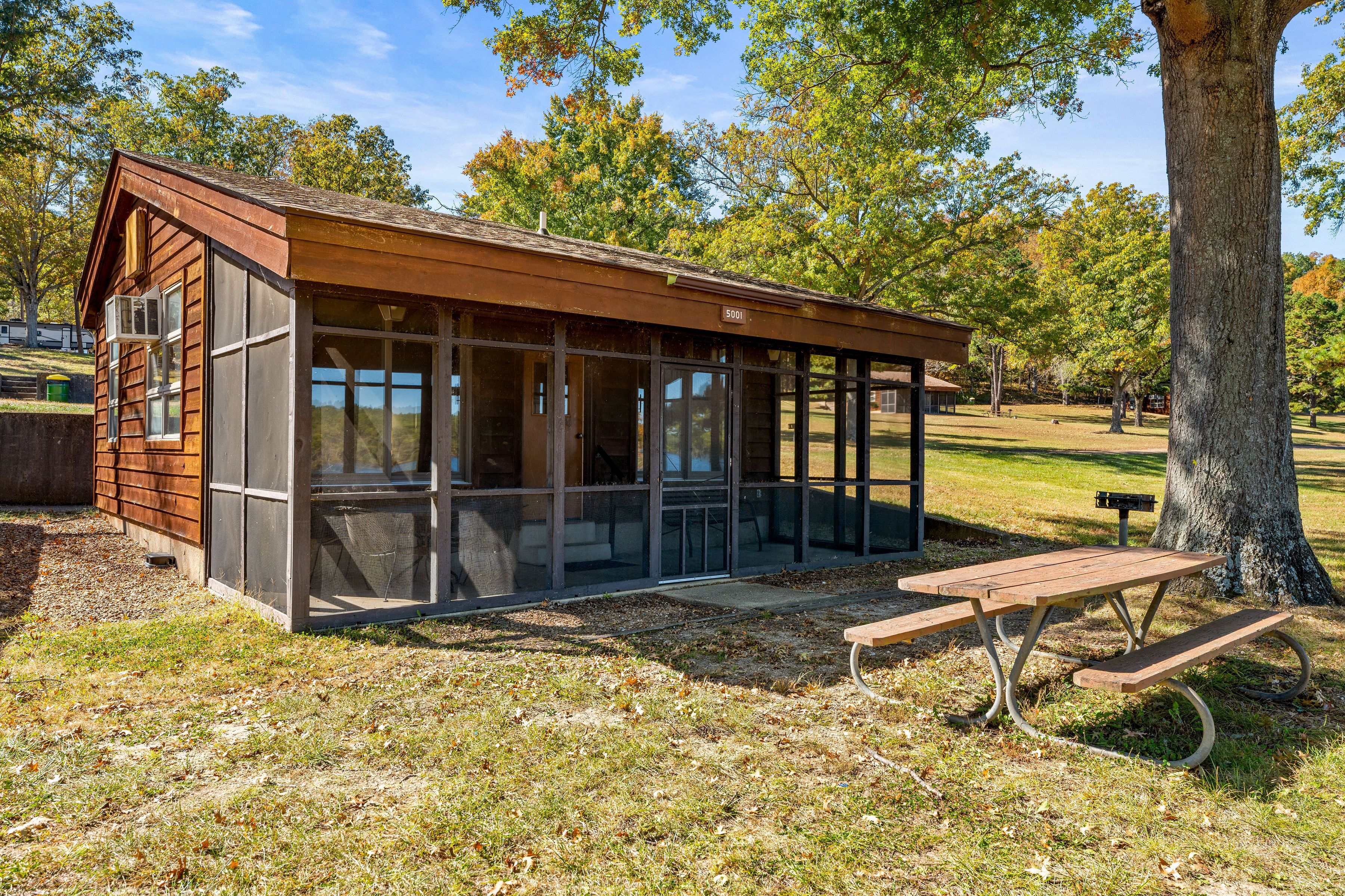 Una pequeña estructura de madera con ventanas amplias, una mesa de picnic y un banco.