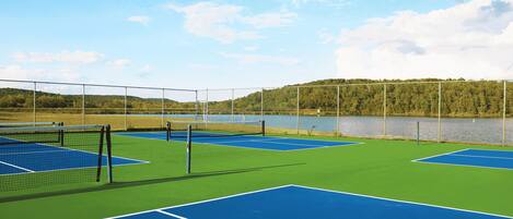 A tennis court with a net, surrounded by a fence, and a lake in the background.