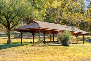 A wooden pavilion with picnic tables and benches, surrounded by trees and grass.