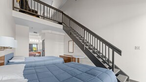 Habitación de hotel con dos camas, una escalera y un baño visible al fondo.