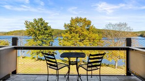 Un balcón con una mesa y dos sillas, con vista a un lago y árboles.