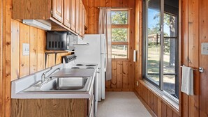A compact kitchen with wooden walls, a white stove, a sink, and a window with a view of the outdoors.
