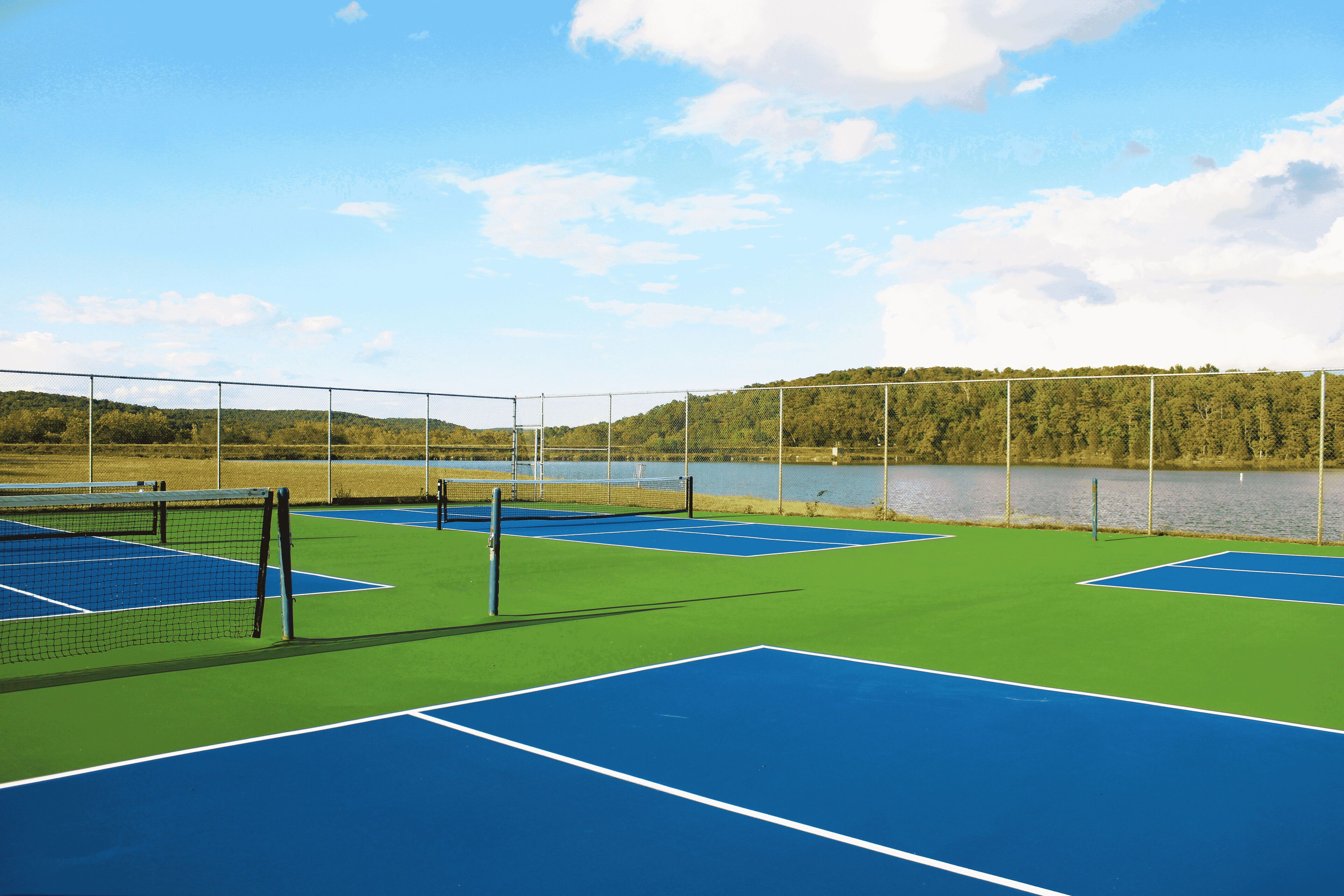 A tennis court with a net, surrounded by a fence, and a lake in the background.