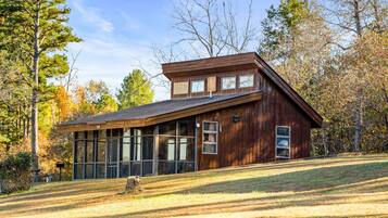 A wooden cabin with large windows, a sloped roof, and a grassy yard.
