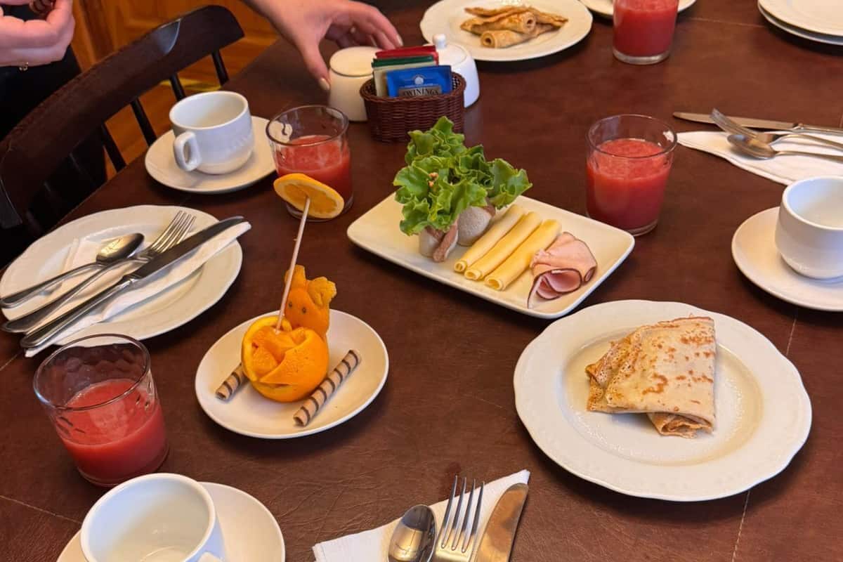Une table à manger dressée avec des assiettes, des couverts et divers aliments, notamment une omelette roulée et un verre de jus rouge.