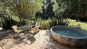 Une terrasse en bois avec un jacuzzi, des fauteuils en osier et une table en verre.
