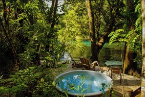 Un bain à remous entouré d’une végétation luxuriante et une terrasse en bois avec des sièges d’extérieur.