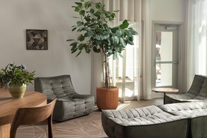 A modern living room with a round wooden table, two grey upholstered sofas, a large potted plant, and a small round table. - Mint House Nashville Marathon Village by Kasa (Nashville)