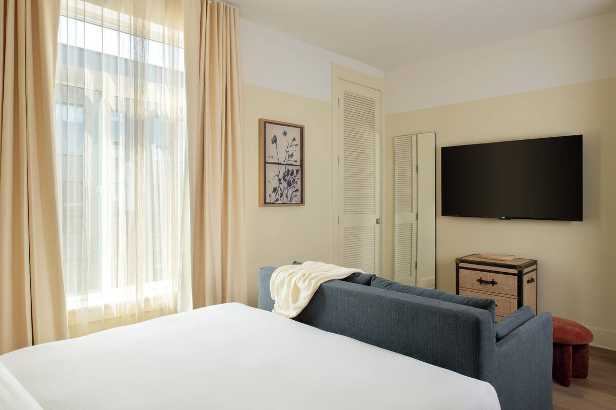 A hotel room with a bed, a sofa, a TV, and a small wooden side table.