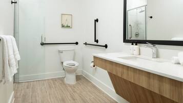 A modern bathroom with a white toilet, a shower with a glass door, a wooden vanity with a sink, and a large mirror.