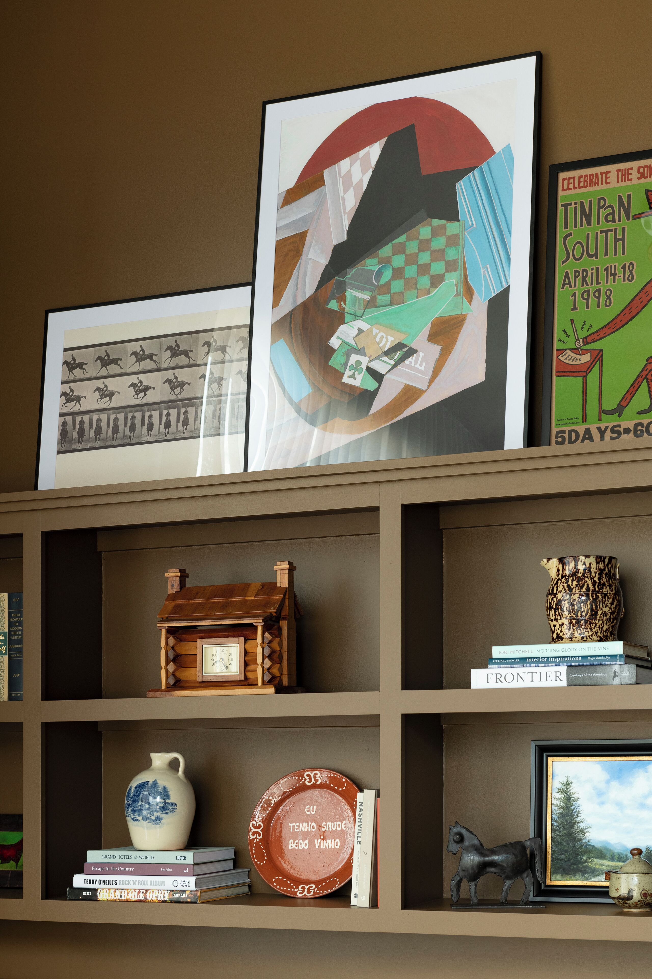 Ein Bücherregal mit verschiedenen Büchern, einem gerahmten Kunstwerk, einer Keramikvase und einem kleinen Hausmodell aus Holz.