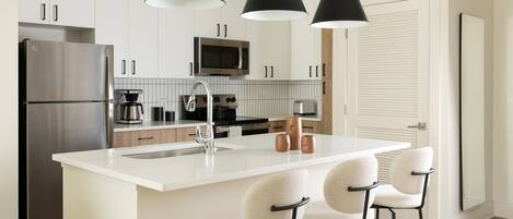 A modern kitchen with a central island, stainless steel appliances, and black pendant lighting.